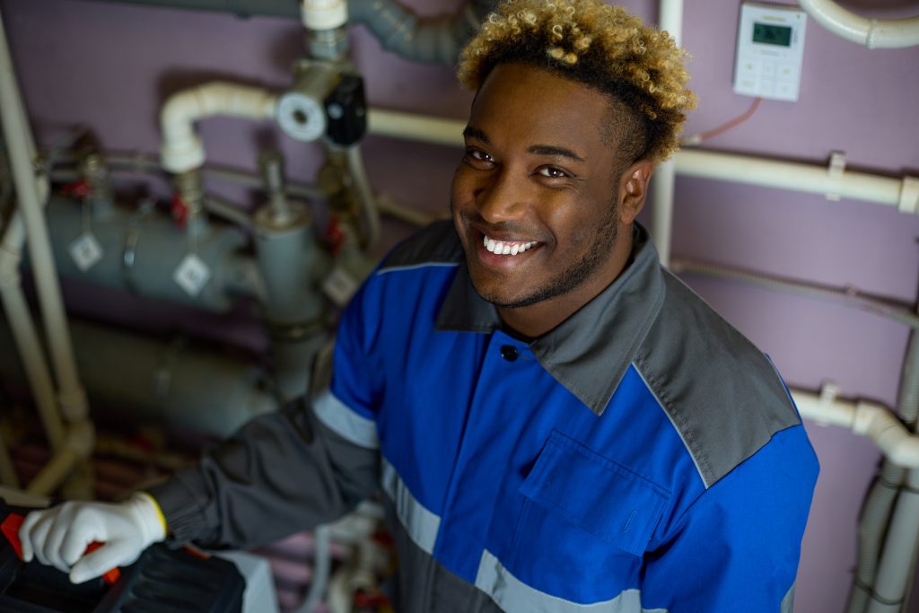 top view of a smiling black worker in overalls standing in the boiler room