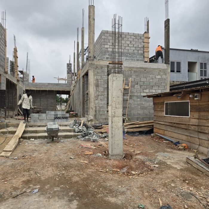 Close-up of a mason carefully spreading mortar between concrete blocks on a building site in Abelemkpe.