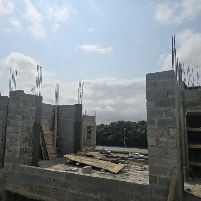 Wide view of active blockwork construction site in Abelemkpe, Accra, showing stacked concrete blocks and rising walls.