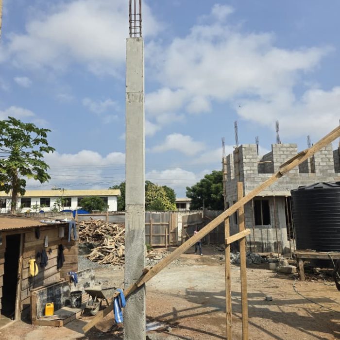 Wide view of active blockwork construction site in Abelemkpe, Accra, showing stacked concrete blocks and rising walls.