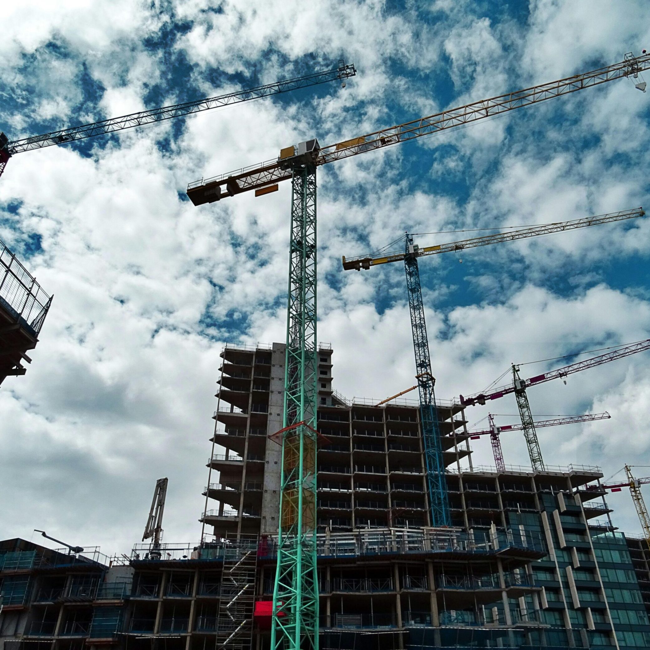 Urban construction site with numerous cranes framing rising skyscrapers against a blue sky.